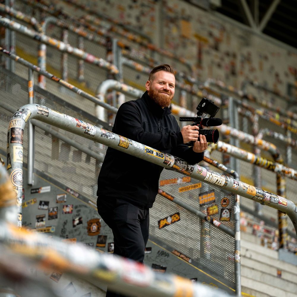 Imagefilm Dreh mit glücklichem Produktionsmitarbeiter, der auf einer Tribüne mit Kamera in der Hand einen Imagefilm filmt