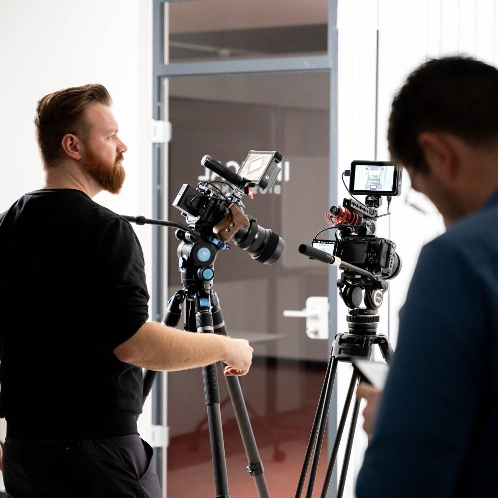 Videoproduktion Dresden Onlinewerbevideo zeigt einen Mitarbeiter der Videoproduktion Onlinewerbevideos beim Kunden, vor ihm stehen zwei professionelle Videokameras auf Stativen, klare Drehsituation im Kundenunternehmen mit technischer Vorbereitung für einen Videodreh
