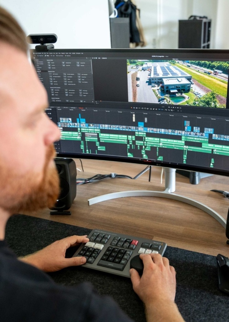 Werbevideo Bearbeitung Ein professioneller Videoersteller sitzt am PC und bearbeitet ein Werbevideo mit Drohnenaufnahme im Videoschnitt