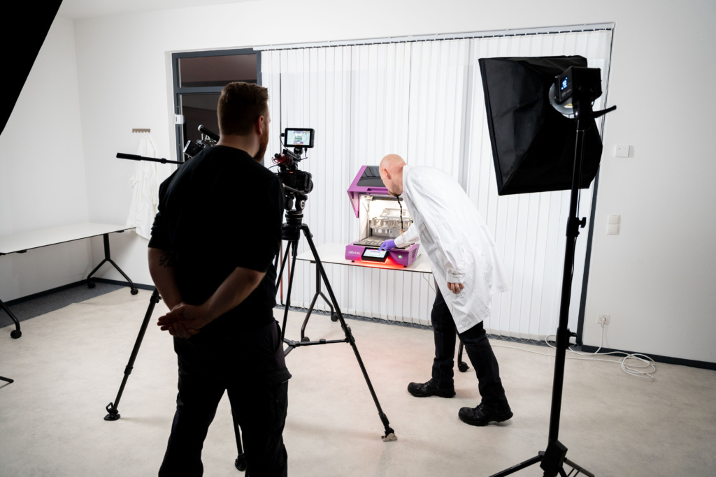 Videoproduktion Dresden Onlinewerbevideo zeigt eine professionelle Videoproduktion direkt beim Kunden, aufgebautes Video Equipment mit Kamera und zwei großen Leuchten, ein Mitarbeiter aus einem Labor erklärt seine Laborgeräte während die Aufnahme im Unternehmen erfolgt