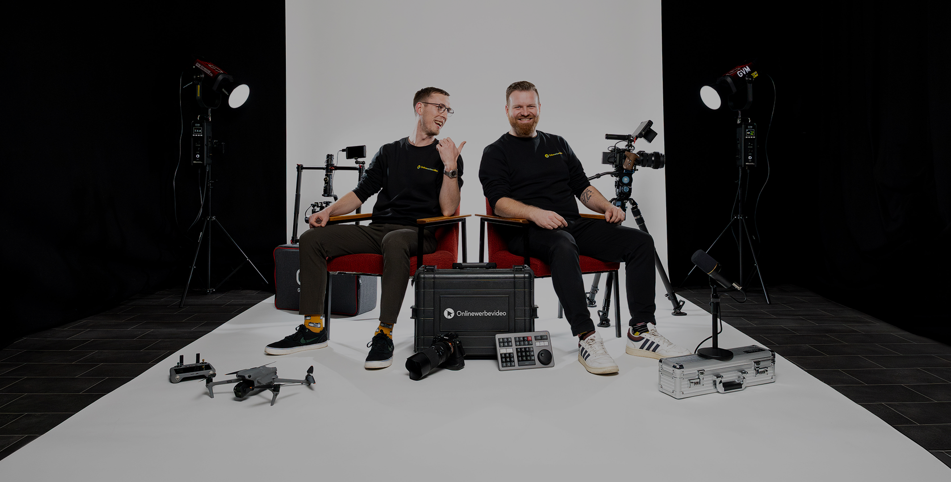 Videoproduktion Dresden Onlinewerbevideo zeigt zwei Männer Philipp Züchner und Stefan Kinzel auf roten Stühlen im Studio, die miteinander lachen, einer schaut in die Kamera, der andere blickt ihn an, natürliche und authentische Szene der Videoproduktion Dresden